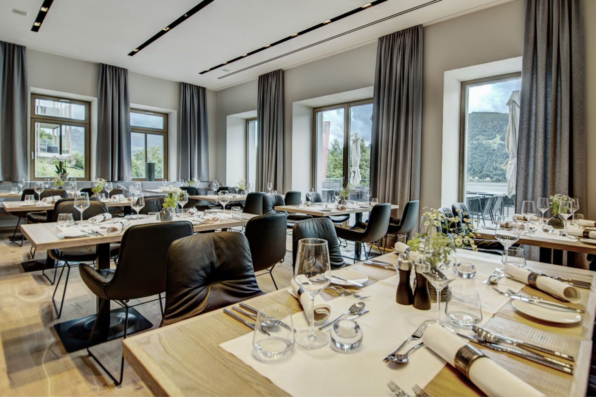 Restaurang på Seehotel Bellevue med täckta bord, svarta stolar och stora fönster med utsikt över gröna kullar 