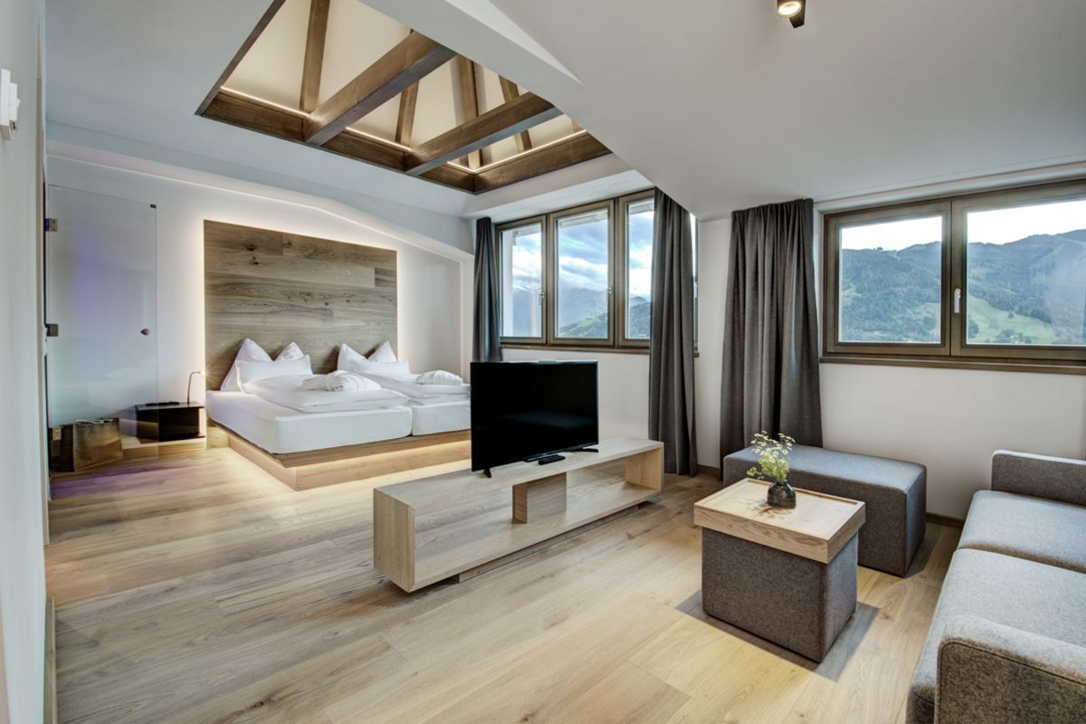 Camera d'albergo con ampio letto matrimoniale, area salotto, TV a schermo piatto e finestre con vista sulle montagne