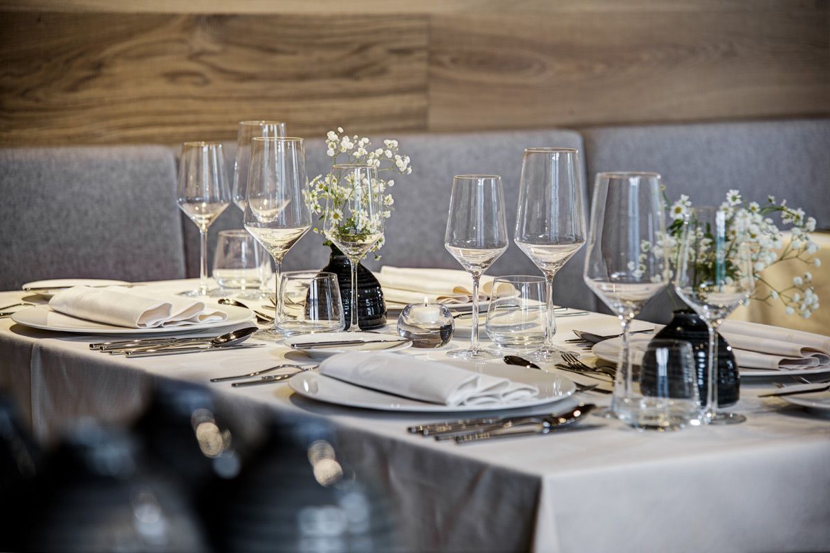 Tavolo da ristorante elegantemente apparecchiato con posate e bicchieri da vino scintillanti davanti a un'accogliente panchina 